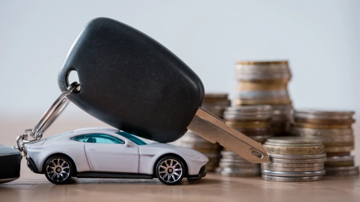 miniature car, car keys and metal coins on wooden surface isolated on grey
