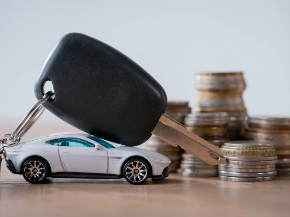 miniature car, car keys and metal coins on wooden surface isolated on grey